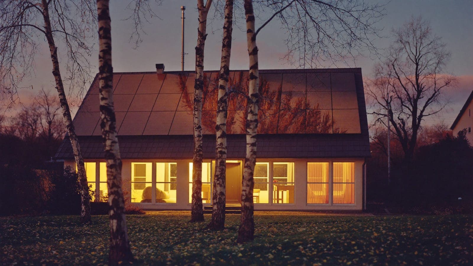 Villa med solpaneler i skymningen, med varmt ljus i alla fönster