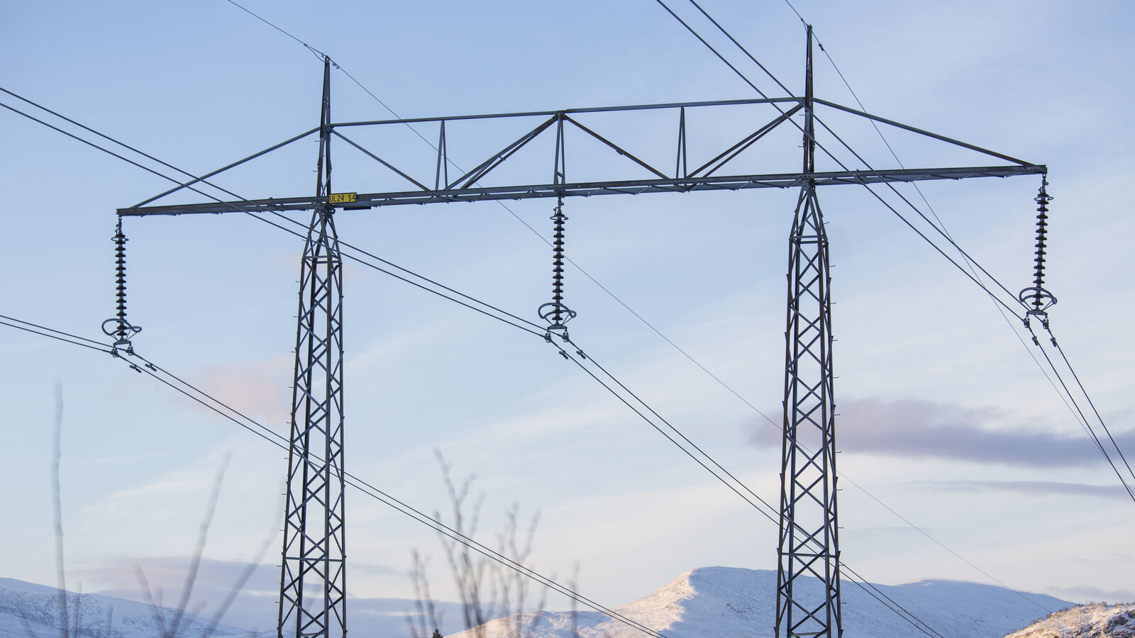 Kraftledningsstolpe i vinterlandskap med snötäckta fjäll i bakgrunden